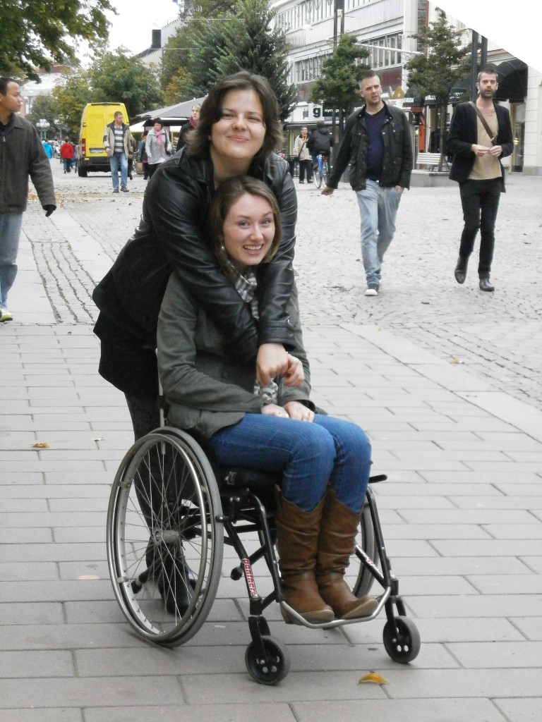Bild på en kram mellan en som står och en som sitter i rullstol.